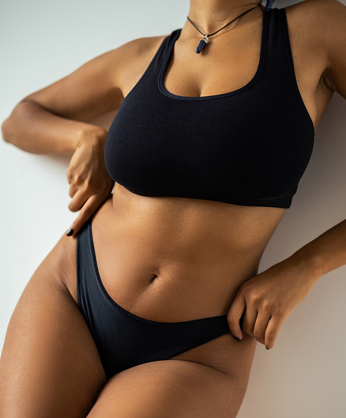 Woman posing in black lingerie against a wall.