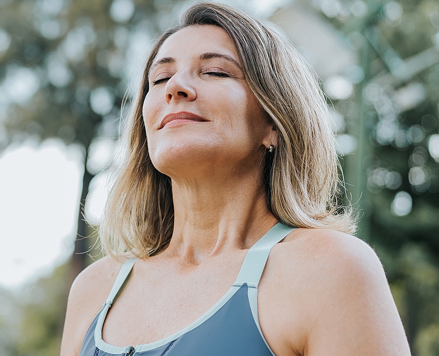 Woman enjoying fresh air outdoors, eyes closed.
