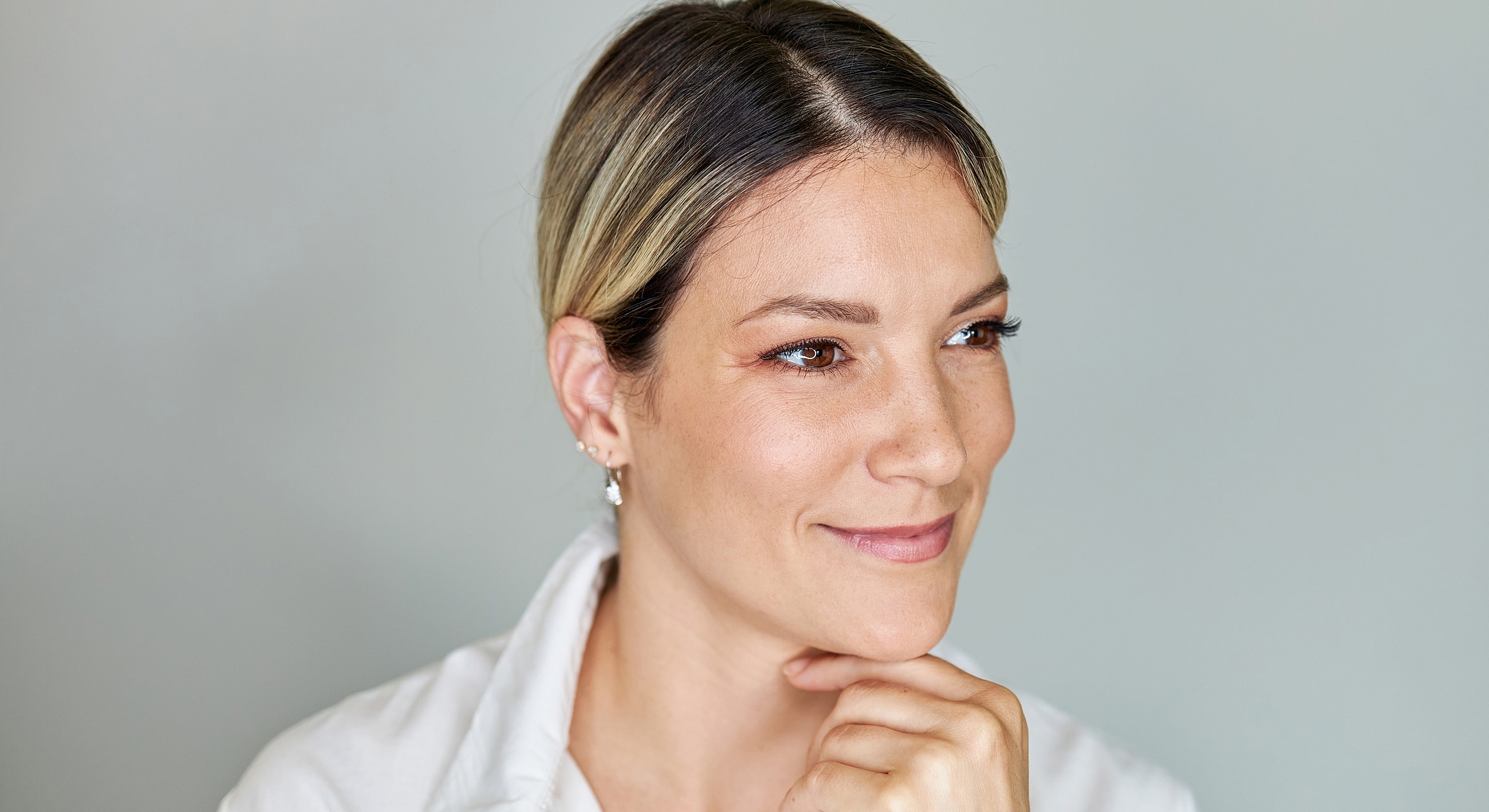 Roswell facials model with chin on hand, thoughtful expression.